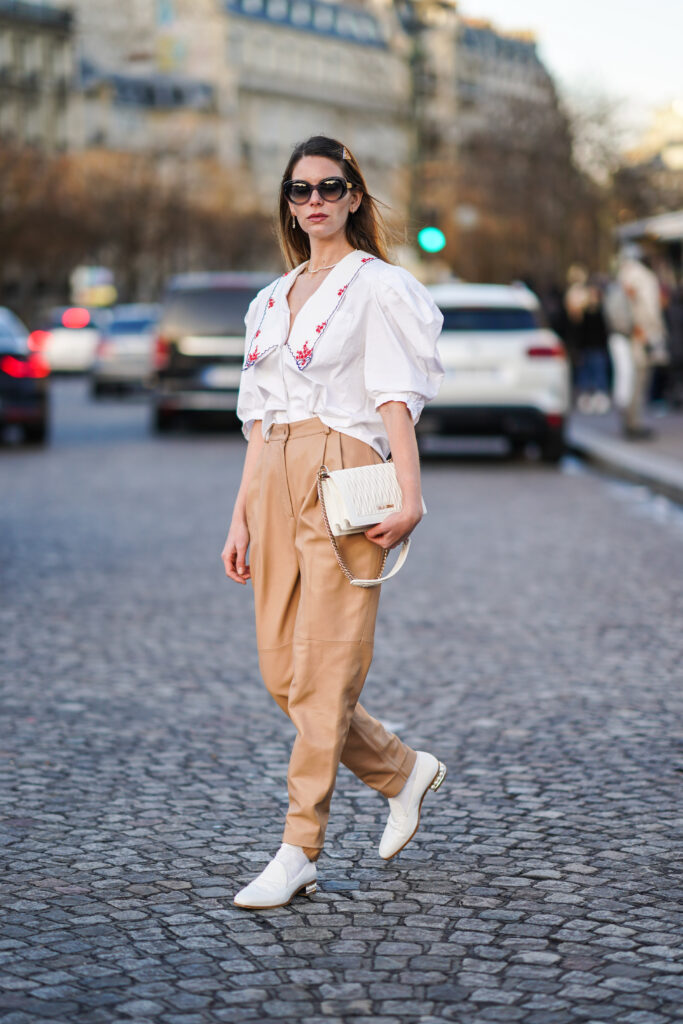 Donna in camicia bianca con ricami, pantaloni beige e loafers bianchi