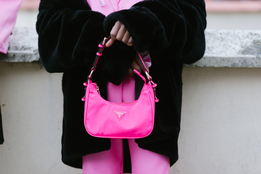 Una borsetta rosa shocking firmata Guess tra le mani di una donna che indossa un cappotto oversize di peluche e una tuta rosa